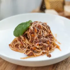Pyszne spaghetti z sosem ragu, posypane parmezanem i udekorowane listkiem bazylii. Idealny przepis na obiad.