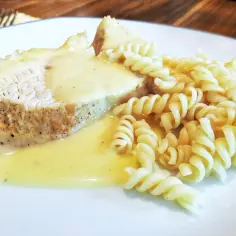 Kawałek mięsa w białym sosie z makaronem fusilli na białym talerzu.