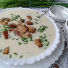 Kremowa zupa porowa z grzankami i szczypiorkiem w białej misce.