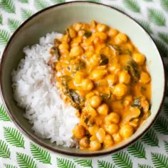 Miseczka z ryżem i aromatycznym curry z ciecierzycy, podane na zielonym, liściastym obrusie.