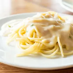 Porcja spaghetti polana kremowym sosem serowym na białym talerzu.