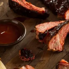 Soczyste żeberka w sosie barbecue, gotowe do podania. Obok miseczka z marynatą do żeberek i pędzelek.