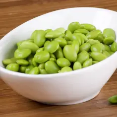Miseczka pełna zielonej fasolki edamame na drewnianym tle.