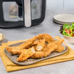Chrupiący kurczak z airfryer na talerzu, obok miseczka sosu i sałatka. Idealny obiad gotowy w mgnieniu oka!