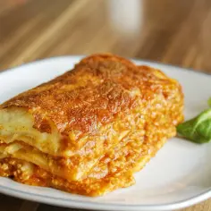 Pyszna, zapieczona lasagne z mięsem mielonym, idealna na prosty obiad. Podana na talerzu z listkami sałaty.
