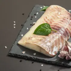Filet surowej ryby z czosnkiem i liśćmi bazylii na czarnej desce.