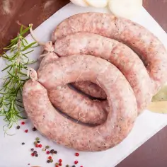 Kiełbasa biała przepis dziadka. Trzy kręgi surowej kiełbasy, gałązka rozmarynu, liście laurowe i kolorowy pieprz.