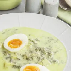 Kremowa zupa szczawiowa z jajkiem na białym talerzu.