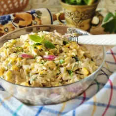 Pyszna sałatka gyros z makaronem orzo, kukurydzą i czerwoną cebulą, udekorowana listkiem bazylii.