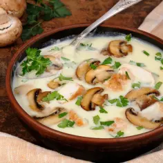 Kremowa zupa pieczarkowa z kurczakiem i natką pietruszki w glinianej misce, obok świeże pieczarki.