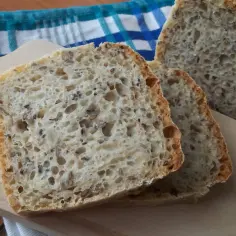 Kromki domowego chleba z ziarnami na desce do krojenia, obok niebiesko-białego ręcznika.