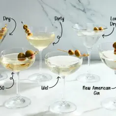 Sześć kieliszków z martini, każdy z oliwkami i etykietami wskazującymi różne warianty.