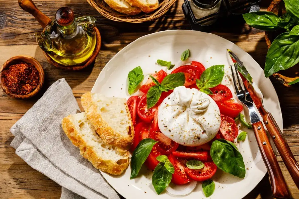 Pyszna burrata co to? Kremowy ser otoczony pomidorami i bazylią, podany z chrupiącym pieczywem i oliwą. Idealna na lekki posiłek.