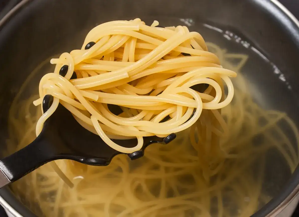 Szczegółowy kadr pokazujący, jak ugotować makaron spaghetti, który jest wyjmowany z wrzącej wody za pomocą czarnej łopatki.