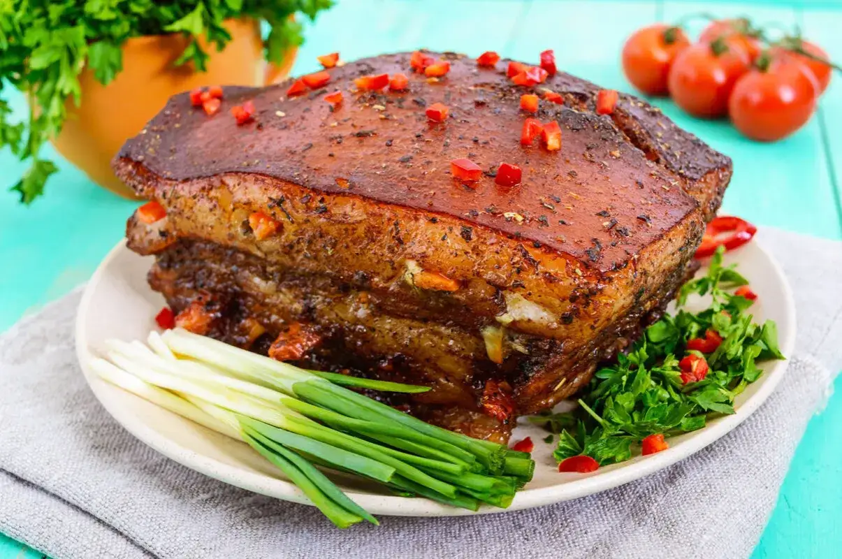 Pyszny boczek pieczony w rękawie, z chrupiącą skórką i soczystym mięsem, ozdobiony papryczką chili i szczypiorkiem.