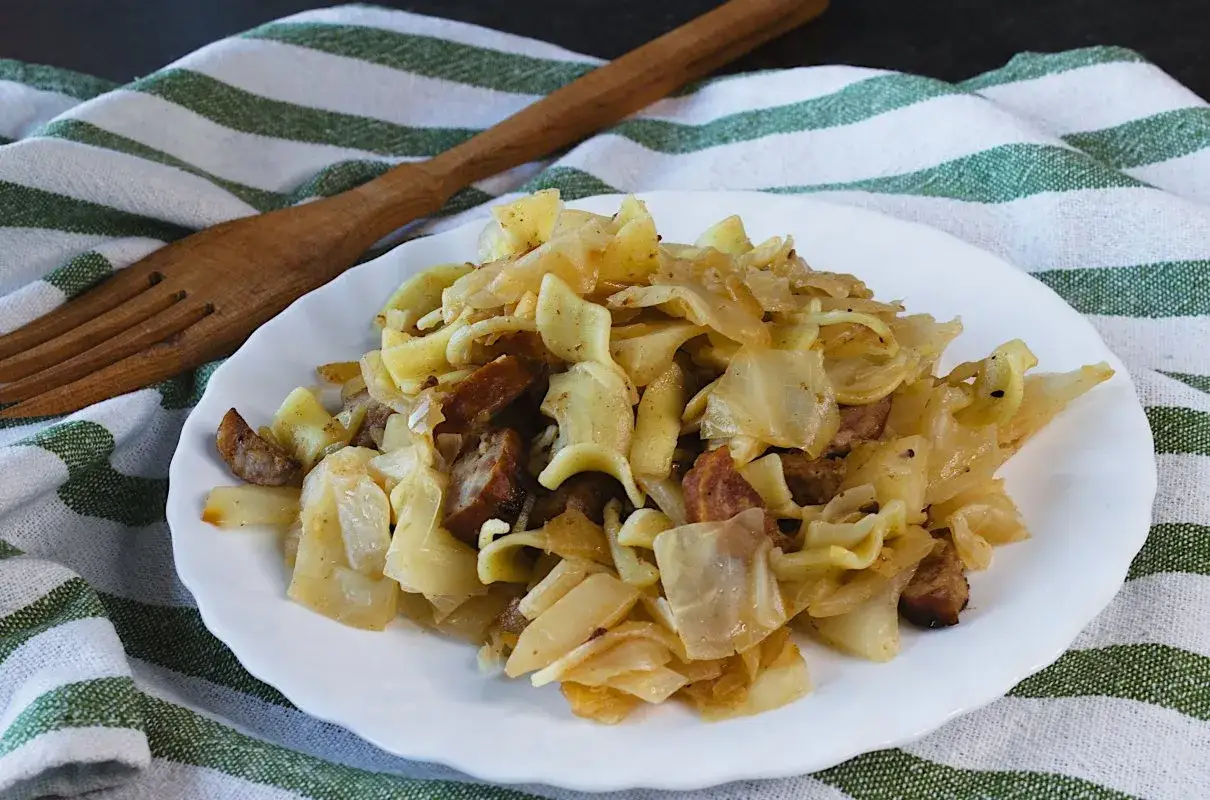 Tradycyjne łazanki z kapustą białą i kiełbasą, podane na talerzu, obok drewnianego widelca.