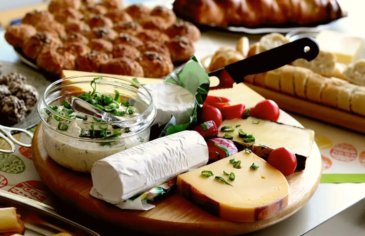 Deska serów z pieczywem i dipem, w tym serek ricotta, pomidorki i zioła.