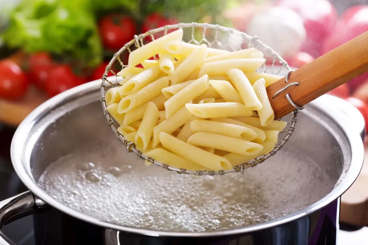 Penne unoszone nad wrzącą wodą w garnku, gotowe do dalszego etapu, jak ugotować makaron.