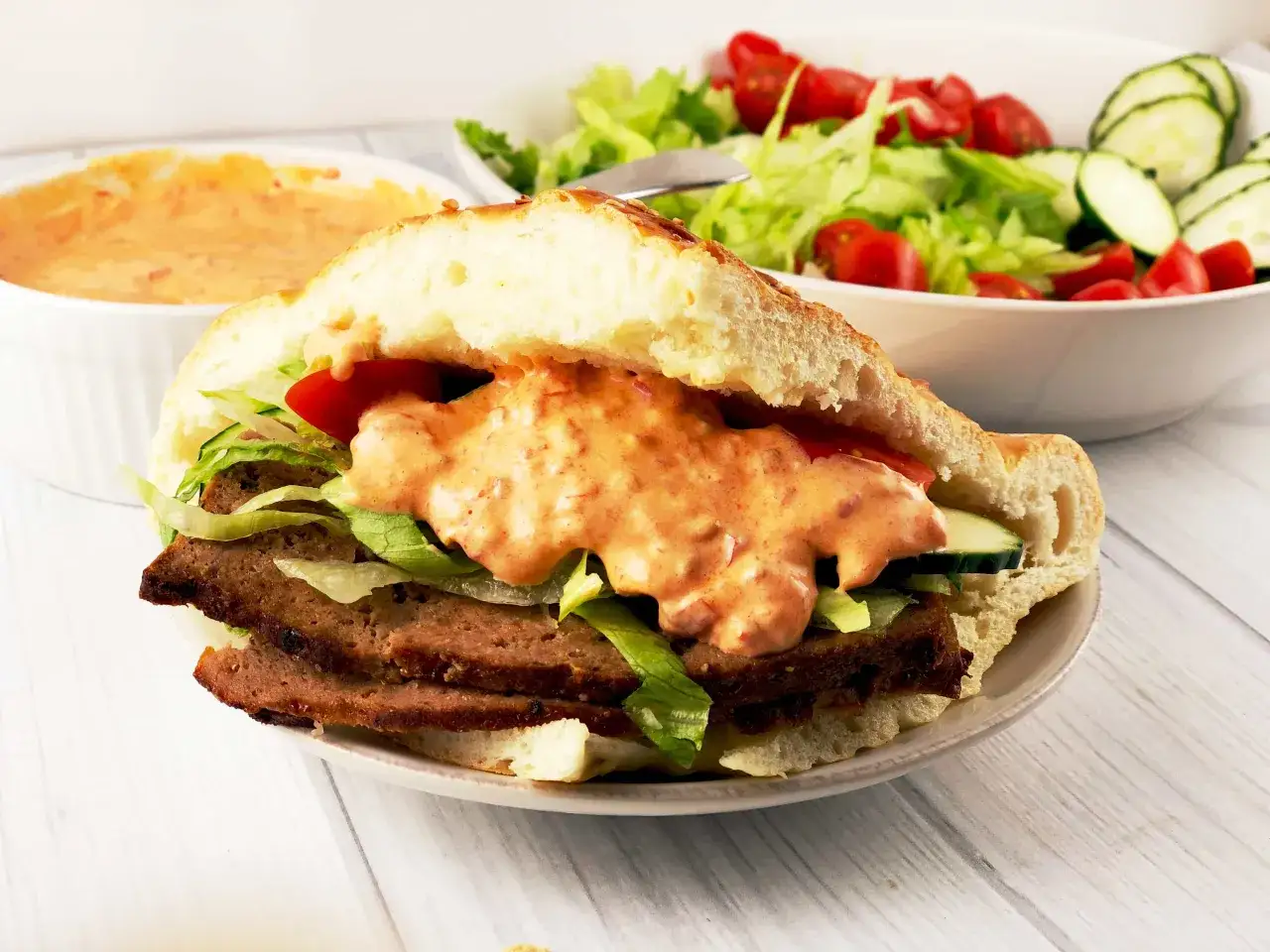 Pyszny kebab w picie z mięsem, warzywami i sosem. Obok miska z sałatką.