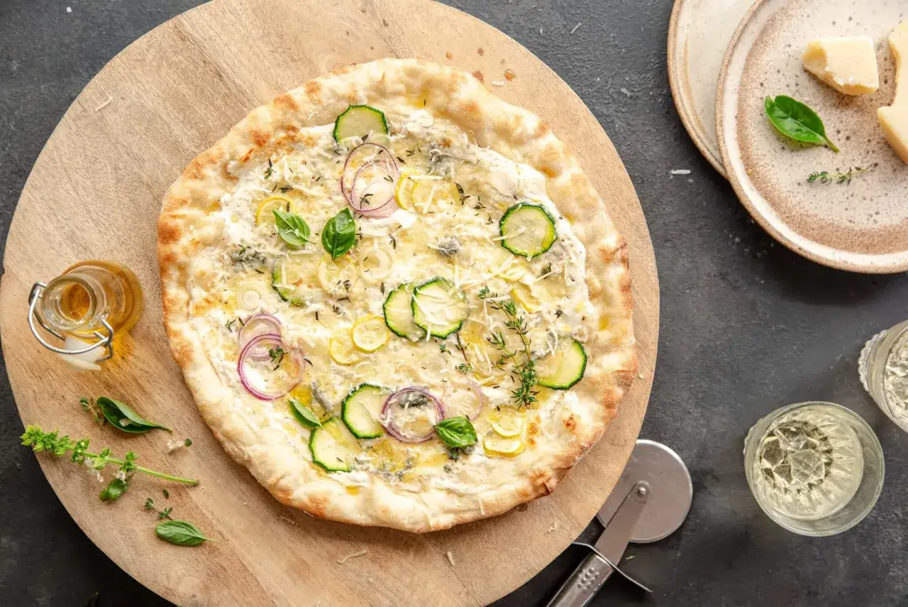 Pyszna pizza bianca z cukinią, cebulą i cytryną, podana na drewnianej desce.