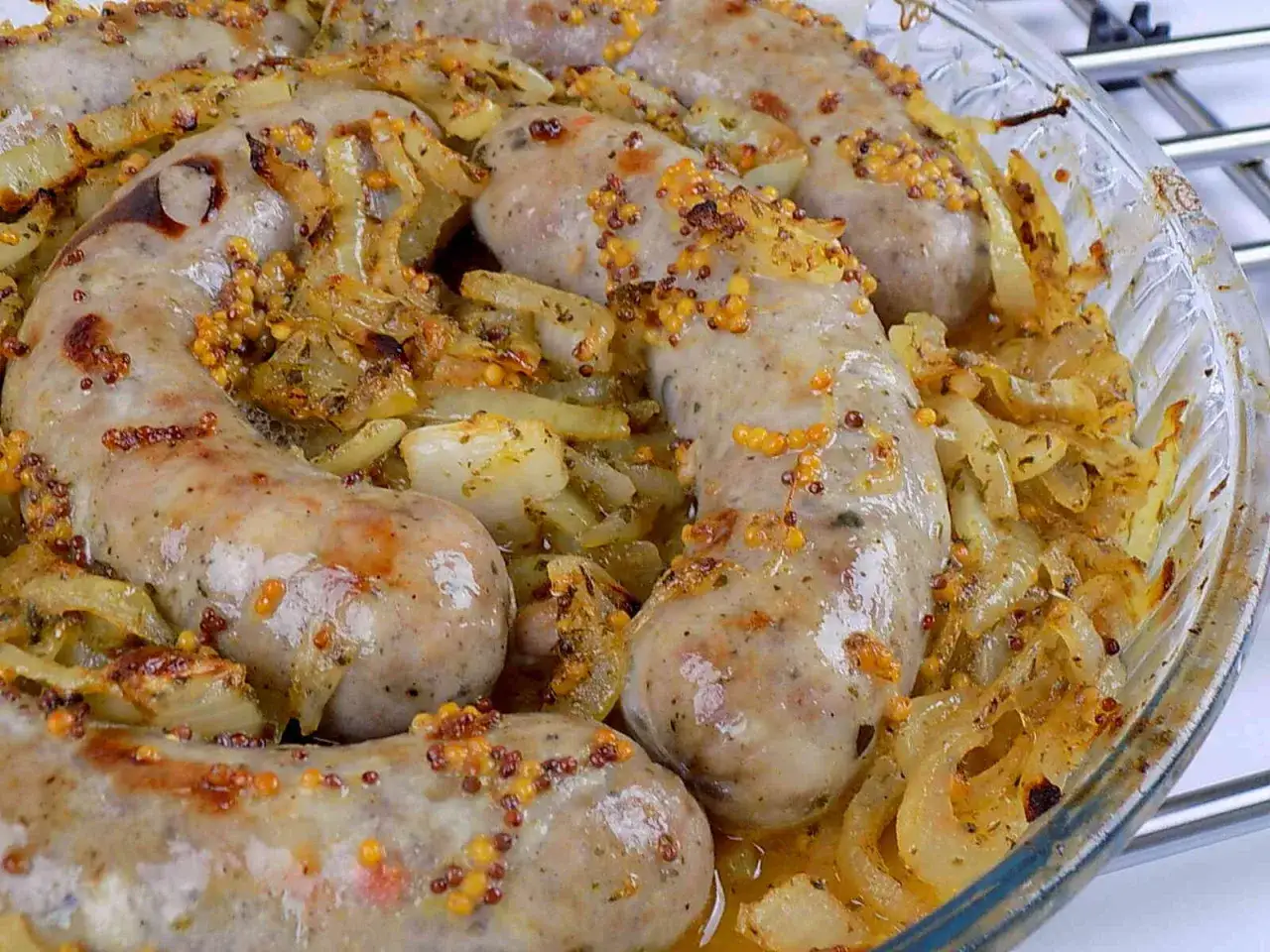 Biała kiełbasa pieczona w cebuli i musztardzie, z widocznymi ziarnami musztardy i przyprawami.