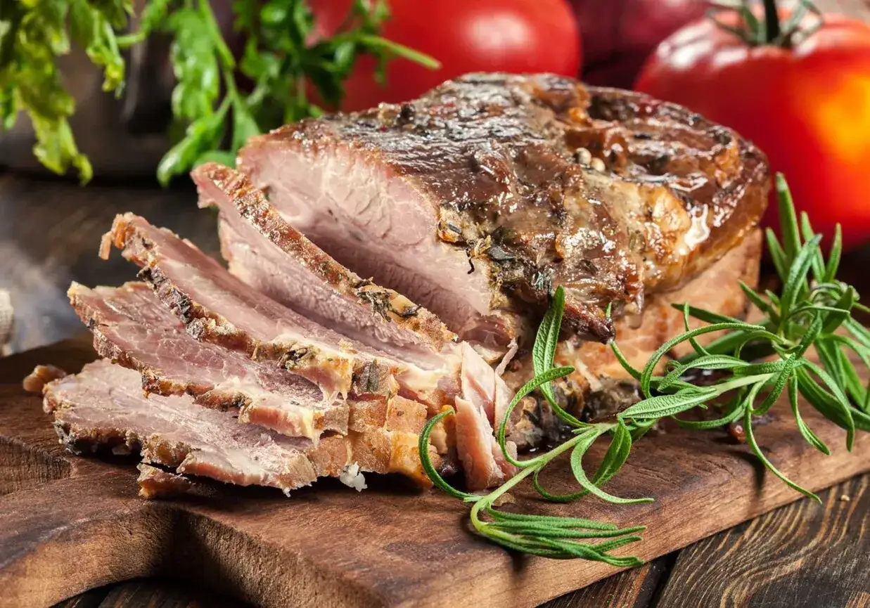 Pyszny boczek pieczony w rękawie, soczysty i aromatyczny, pokrojony na desce z rozmarynem i pomidorami.
