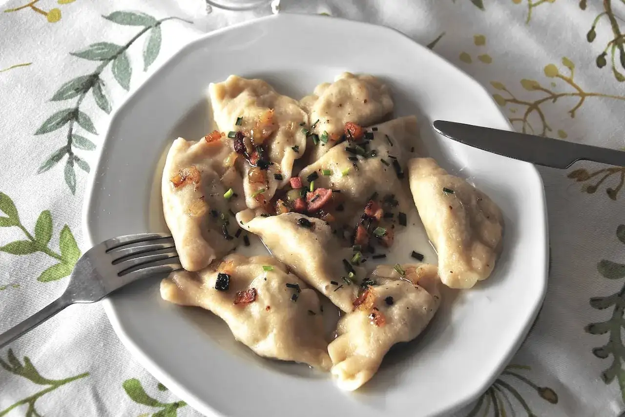 Pyszne pierogi ukraińskie, polane skwarkami i posypane szczypiorkiem, czekają na widelcu.