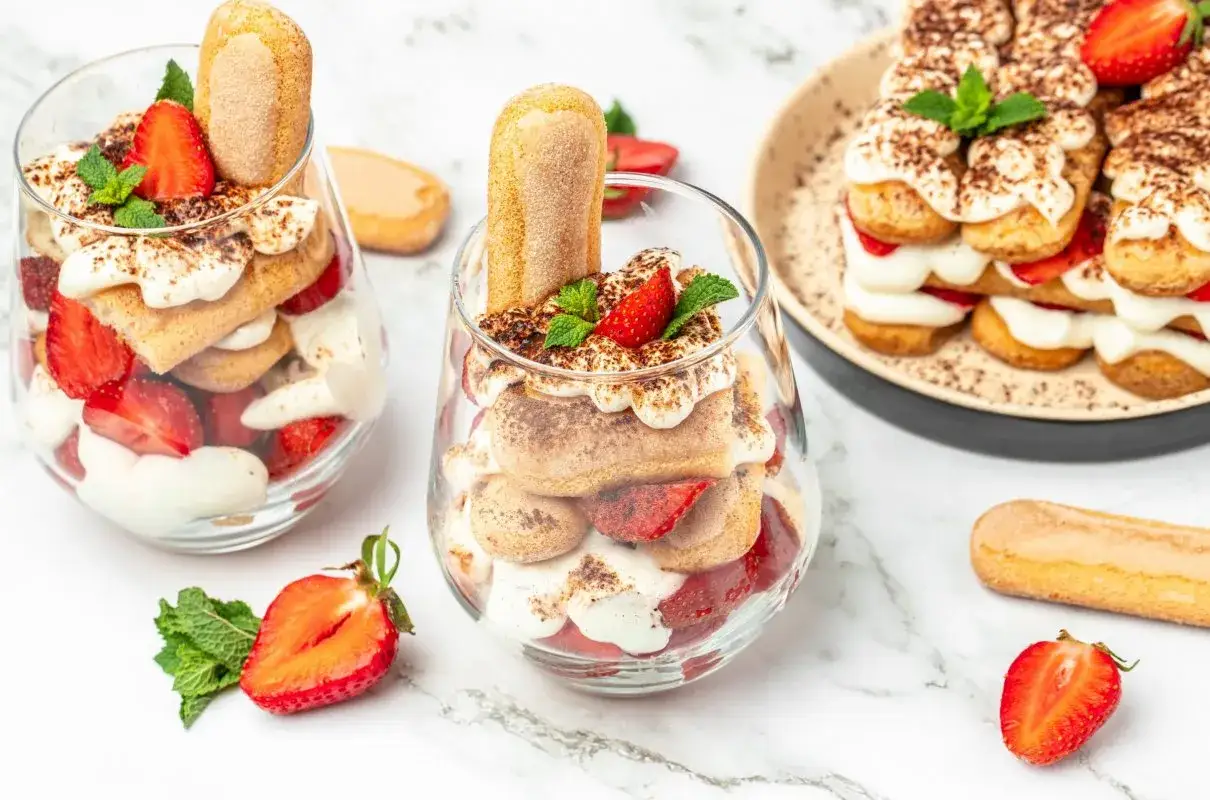 Pyszny deser z mascarpone, biszkoptów i truskawek w pucharkach i na talerzu.