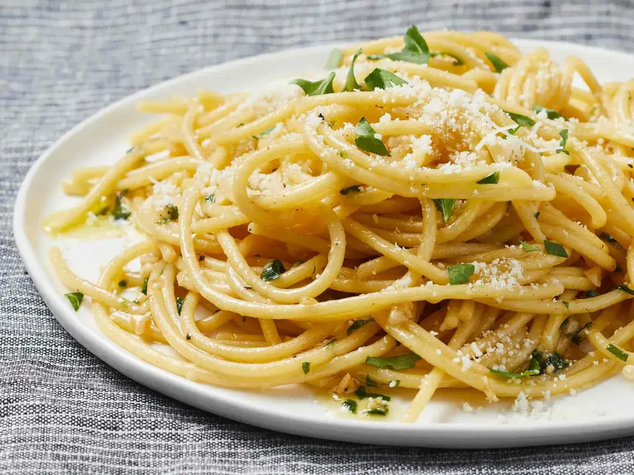 Szybki obiad z makaronem: złociste spaghetti z parmezanem i natką pietruszki, polane oliwą. Idealne na szybki posiłek.