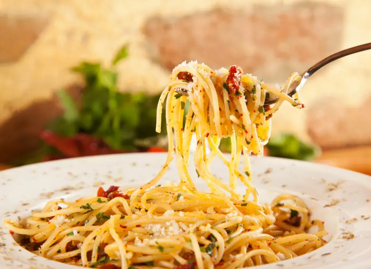 Widok z bliska na talerz spaghetti z widelcem unoszącym porcję. Danie jest posypane parmezanem i ziołami, co sugeruje, jakie przyprawy do spaghetti są najlepsze.