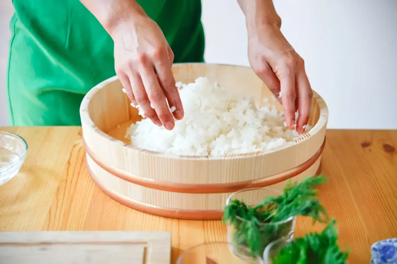 Dłonie mieszają ryż do sushi w drewnianej kadzi.