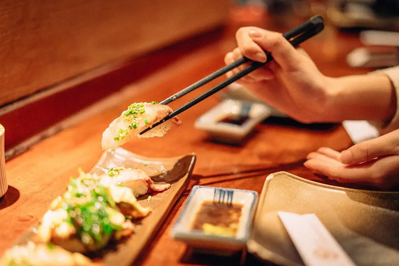 Dłoń pokazuje, jak trzymać pałeczki do sushi, podnosząc kawałek nigiri.