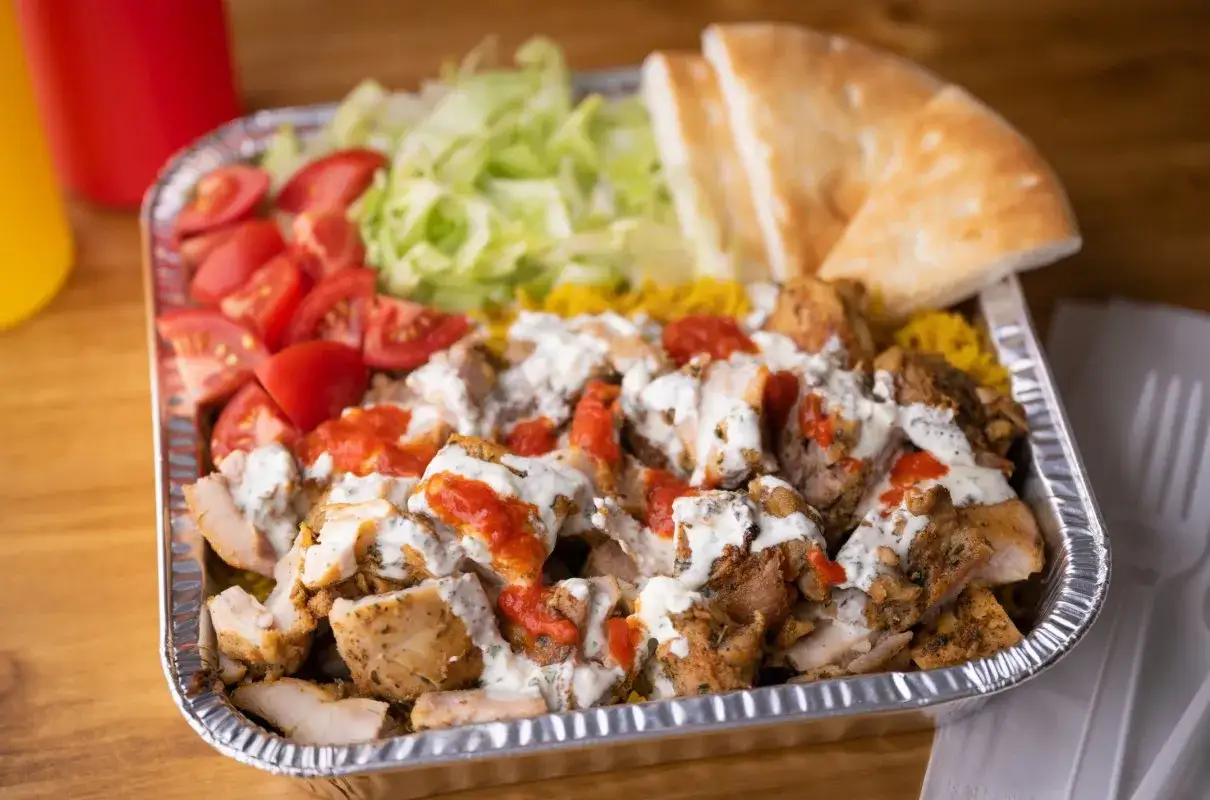 Pyszna shoarma drobiowa z ryżem, pomidorami, sałatą i sosem, podana w aluminiowej tacce. Idealna na szybki posiłek.