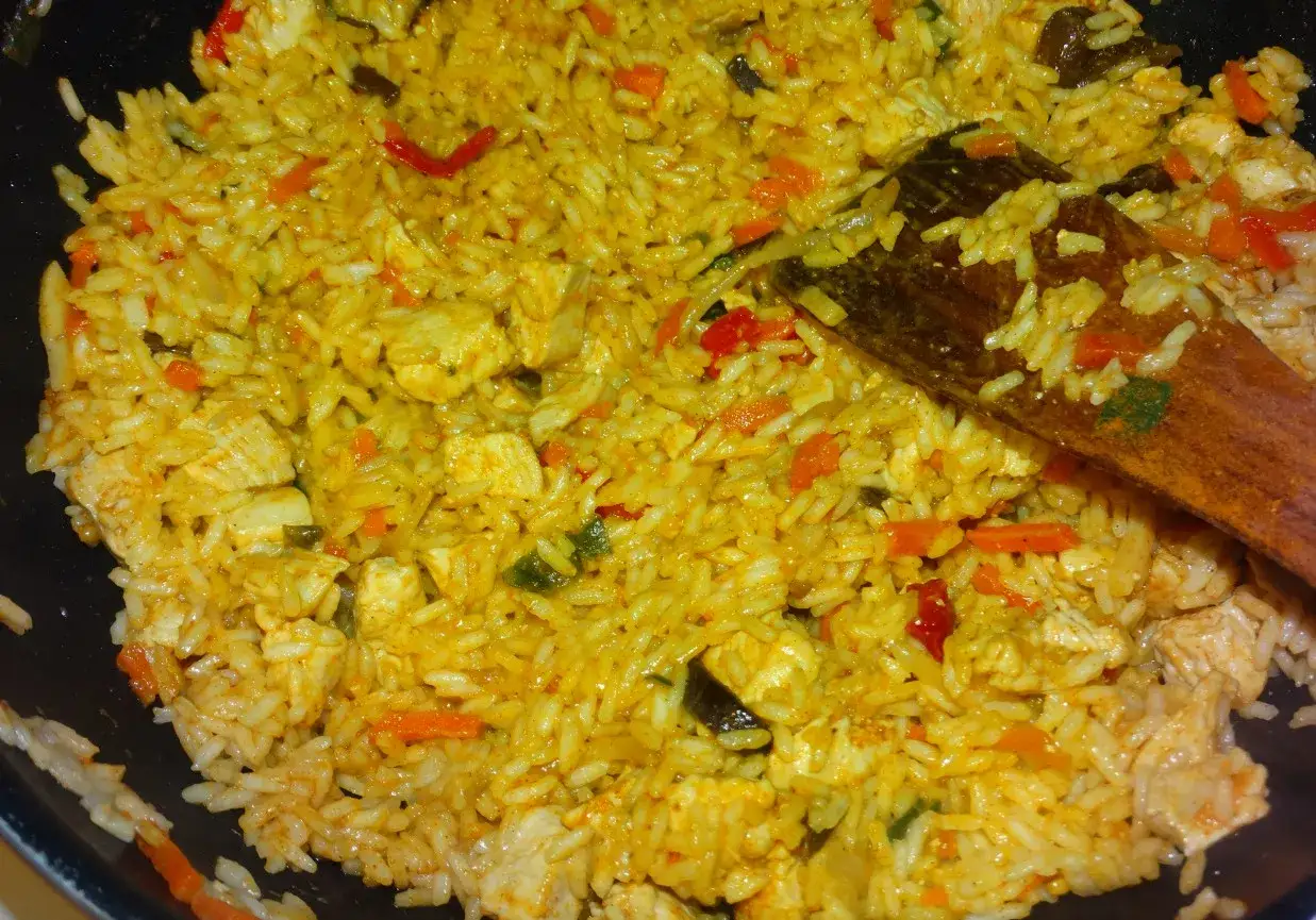 Pyszny ryż z kurczakiem i warzywami, doprawiony aromatycznym curry. Drewniana łopatka miesza danie.