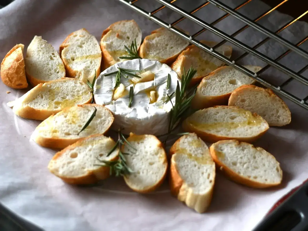Pyszny camembert z grilla, otoczony kromkami bagietki z rozmarynem i czosnkiem, czeka na zapieczenie.