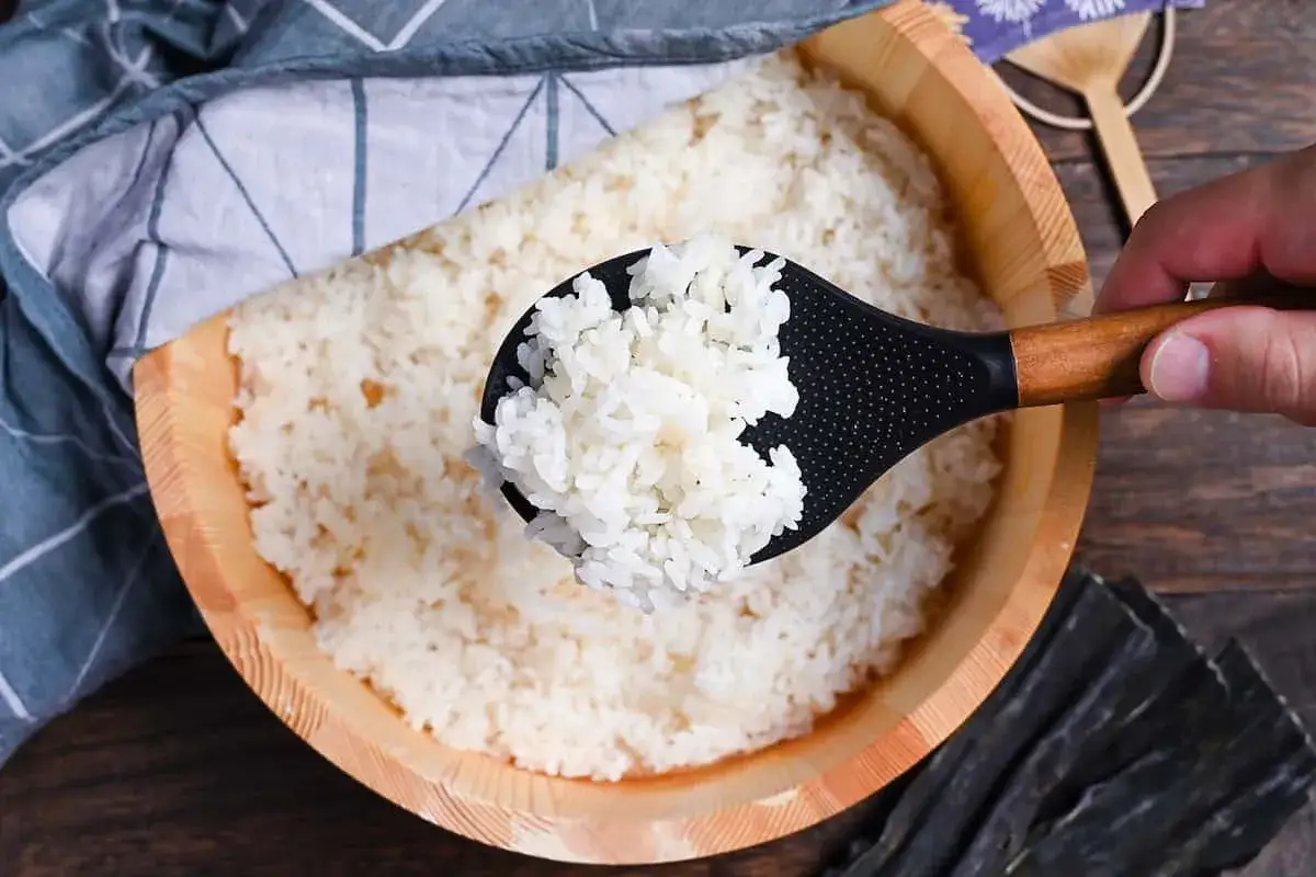 Łyżka nabiera idealny ryż do sushi z drewnianego naczynia. Obok leży kawałek wodorostów.