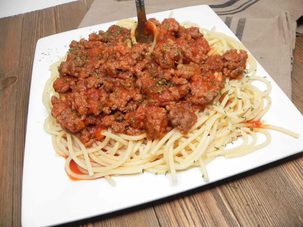 Pyszny przepis na makaron z sosem bolognese, bogaty w mięso mielone i pomidory, posypany ziołami.