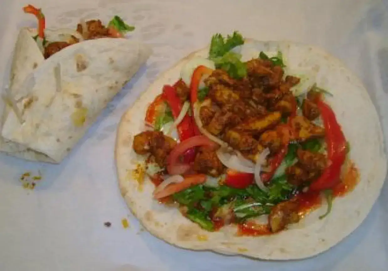 Pyszny kebab w tortilli z kurczakiem, warzywami i sosem. Obok leży zwinięty w rulon kebab.