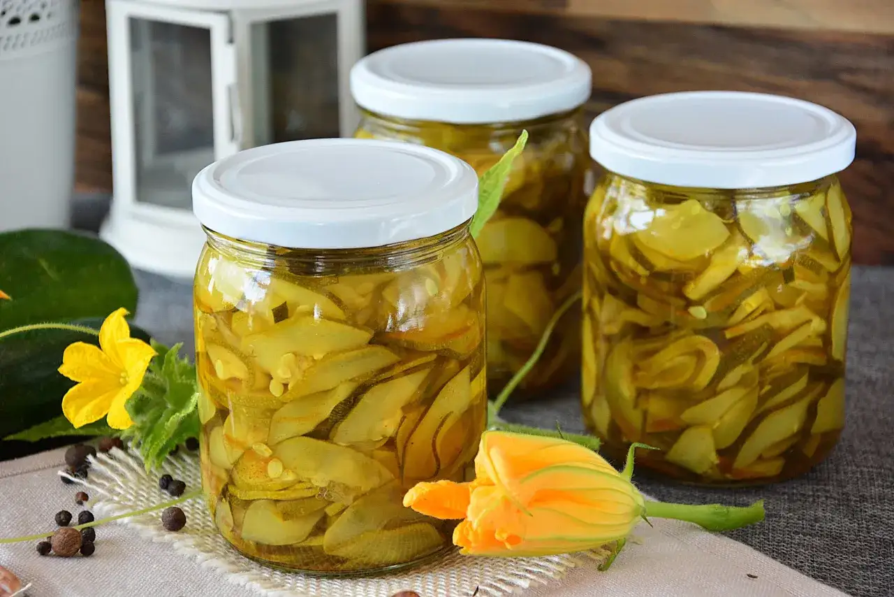 Słoiki z cukinią w zalewie słodko-kwaśnej z curry, ozdobione kwiatami cukinii i przyprawami.
