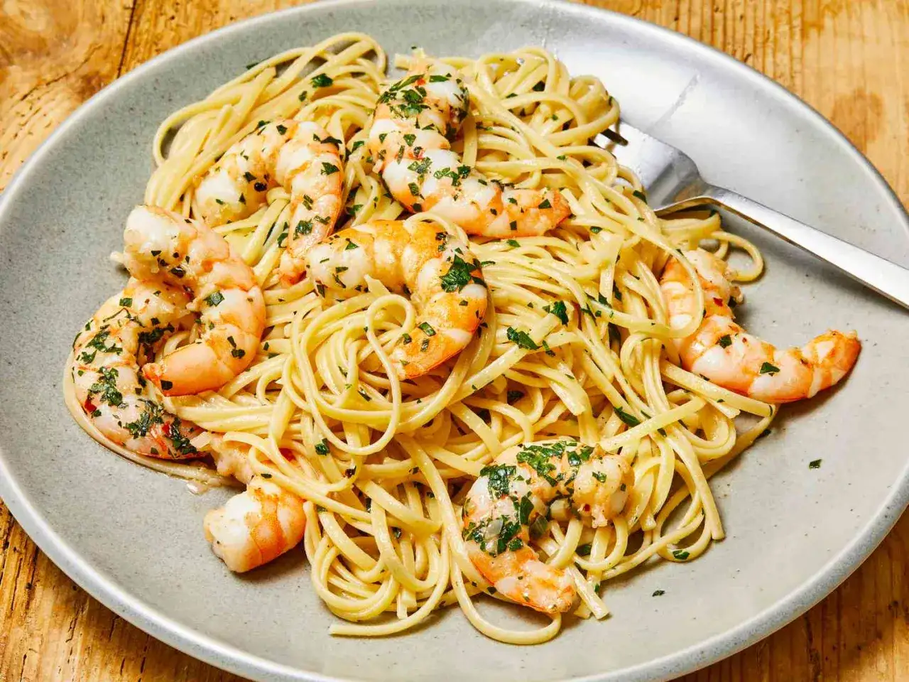 Pyszne włoskie dania: linguine z krewetkami i natką pietruszki, podane na szarym talerzu.
