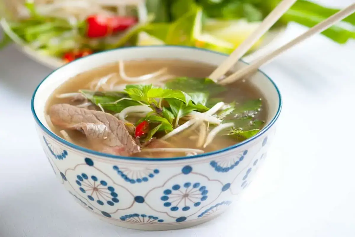 Aromaticzne pho z wołowiną, makaronem ryżowym, kiełkami i świeżą miętą w ozdobnej misce.