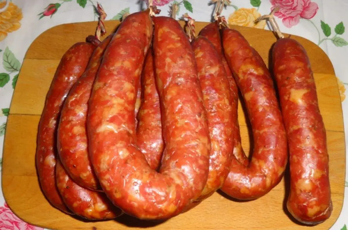 Prawdziwa wiejska kiełbasa przepis na domową wędlinę. Kilka pętelek wędzonej kiełbasy na drewnianej desce.