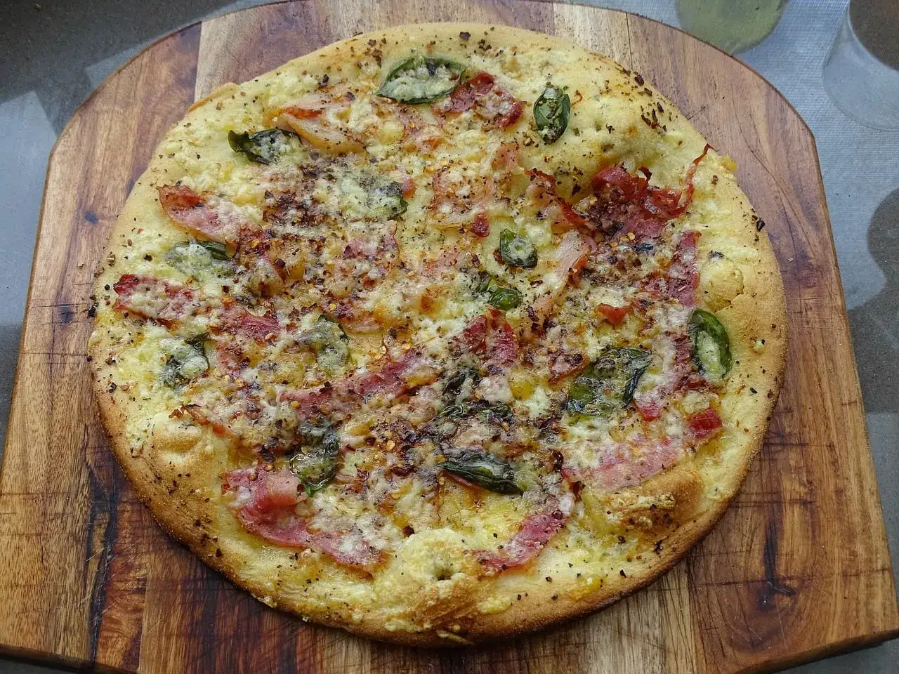 Pyszna pizza bianca z bekonem, serem i zielonymi papryczkami, posypana płatkami chili, na drewnianej desce.