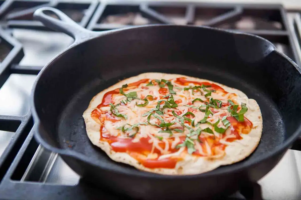 Szybka pizza z tortilli na patelni, z sosem pomidorowym, serem i bazylią, gotowa do podania.