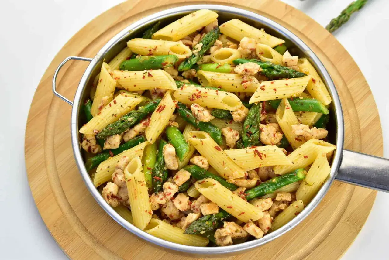 Penne z kurczakiem i szparagami, posypane papryką. Pyszne danie na talerzu.