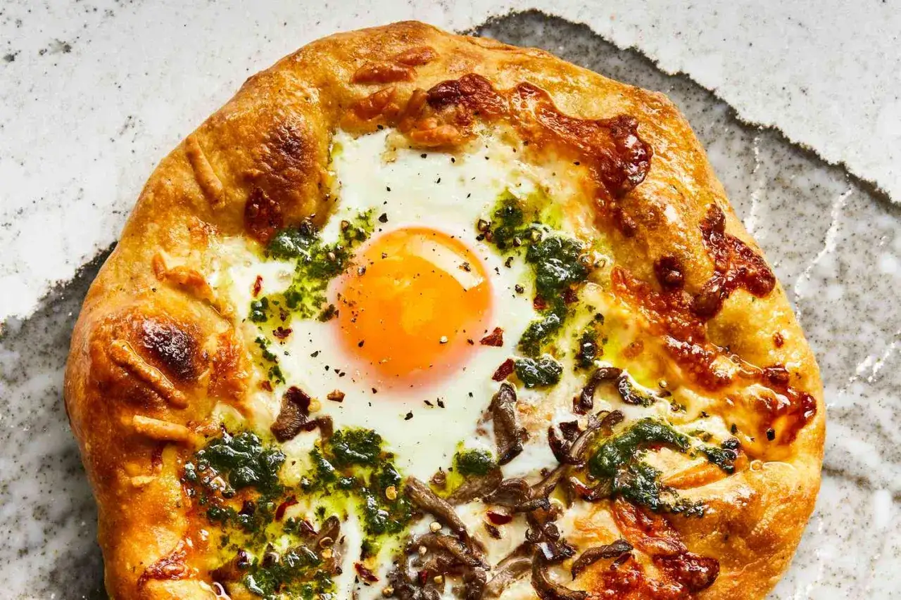 Apetyczna pizza z jajkiem na środku, otoczona chrupiącym ciastem, serem i zielonym sosem. Idealna na śniadanie lub brunch.