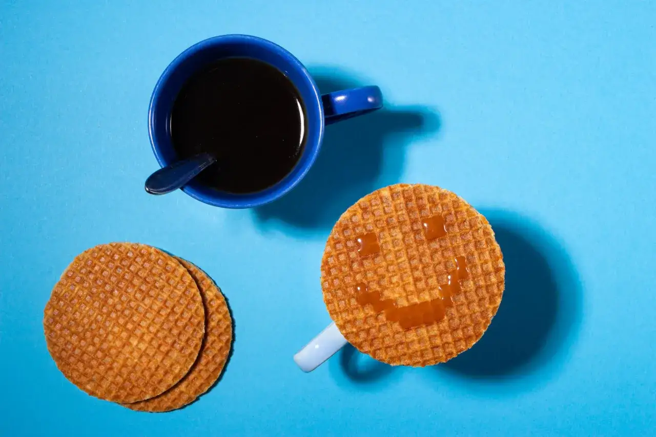 Uśmiechnięte wafle holenderskie z karmelem i filiżanka kawy na niebieskim tle. Idealny poranek z holenderskimi przysmakami.