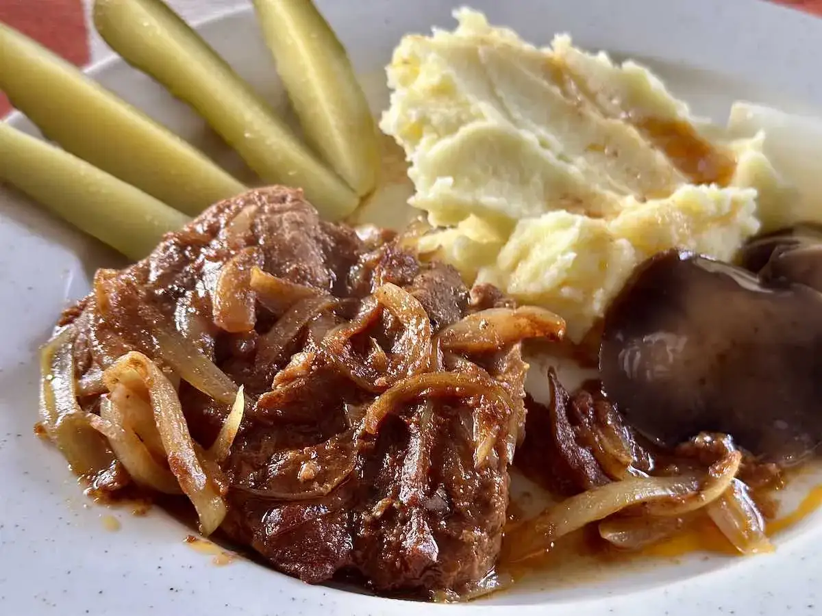 Rozpływająca się karkówka z piekarnika z cebulką, puree ziemniaczane, ogórki kiszone i pieczarka.