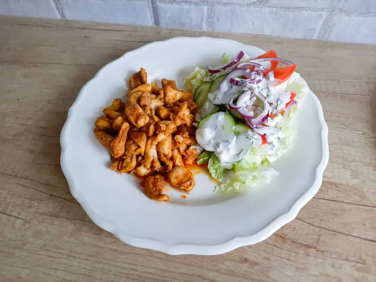 Pyszna shoarma drobiowa z chrupiącą sałatką, pomidorem, ogórkiem i sosem czosnkowym na białym talerzu.
