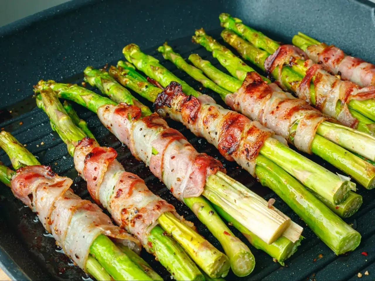 Zielone szparagi owinięte w chrupiący boczek, przygotowywane na grillu. Pyszne szparagi z grilla kuszą aromatem.